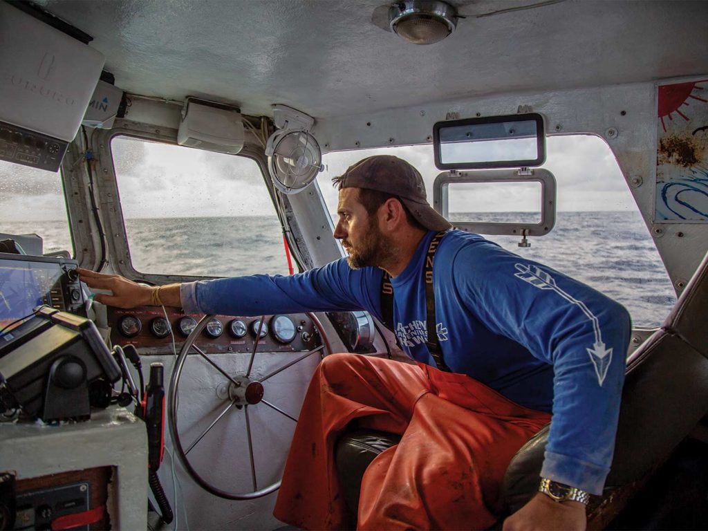 A sport-fishing captain examines equipment while piloting the boat.