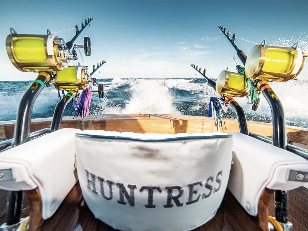 Four heavy-duty sport-fishing reels attached to a fighting chair on a sport-fishing boat deck.