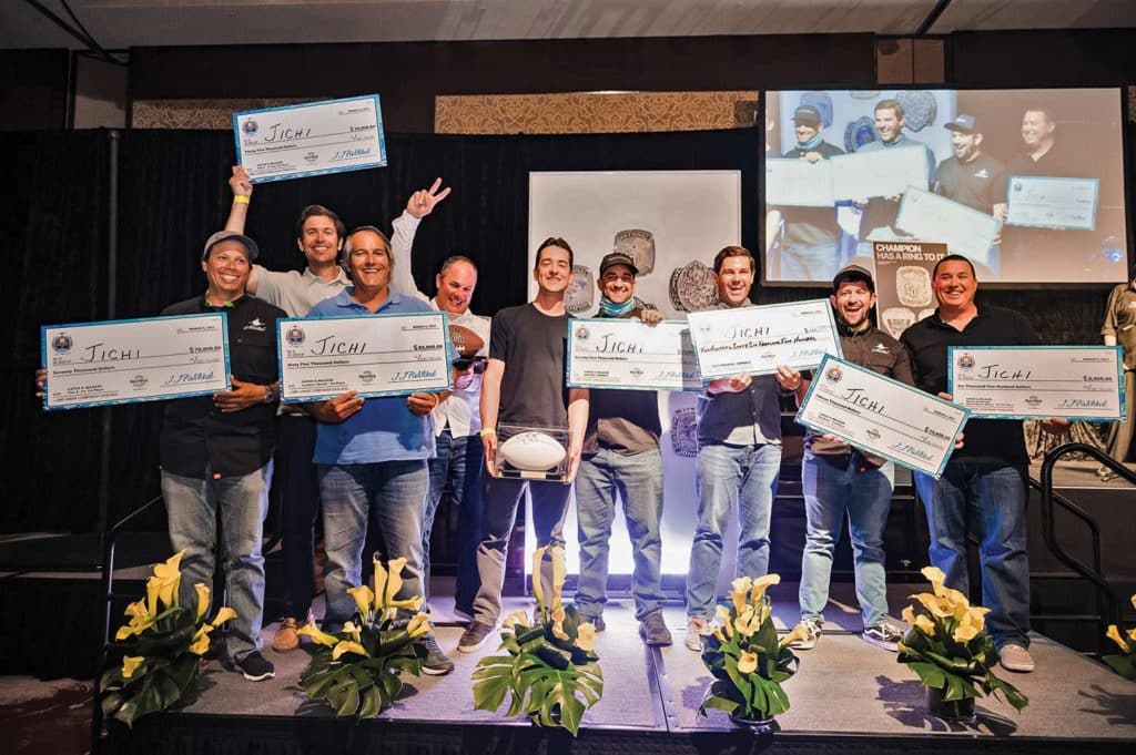 A fishing team holds up printed checks and celebrates on stage.