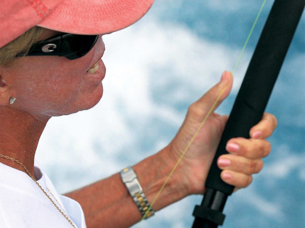 A woman fishing on the back of a boat deck.