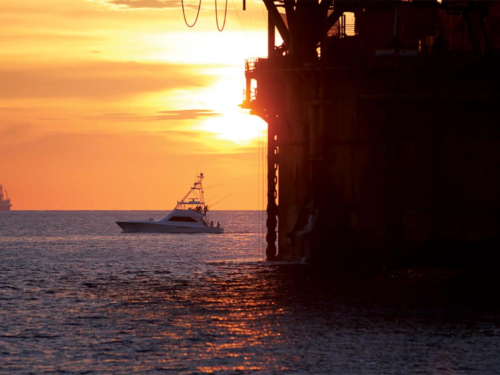 A sunset overlooking the ocean and an offshore rig and fishing boat.