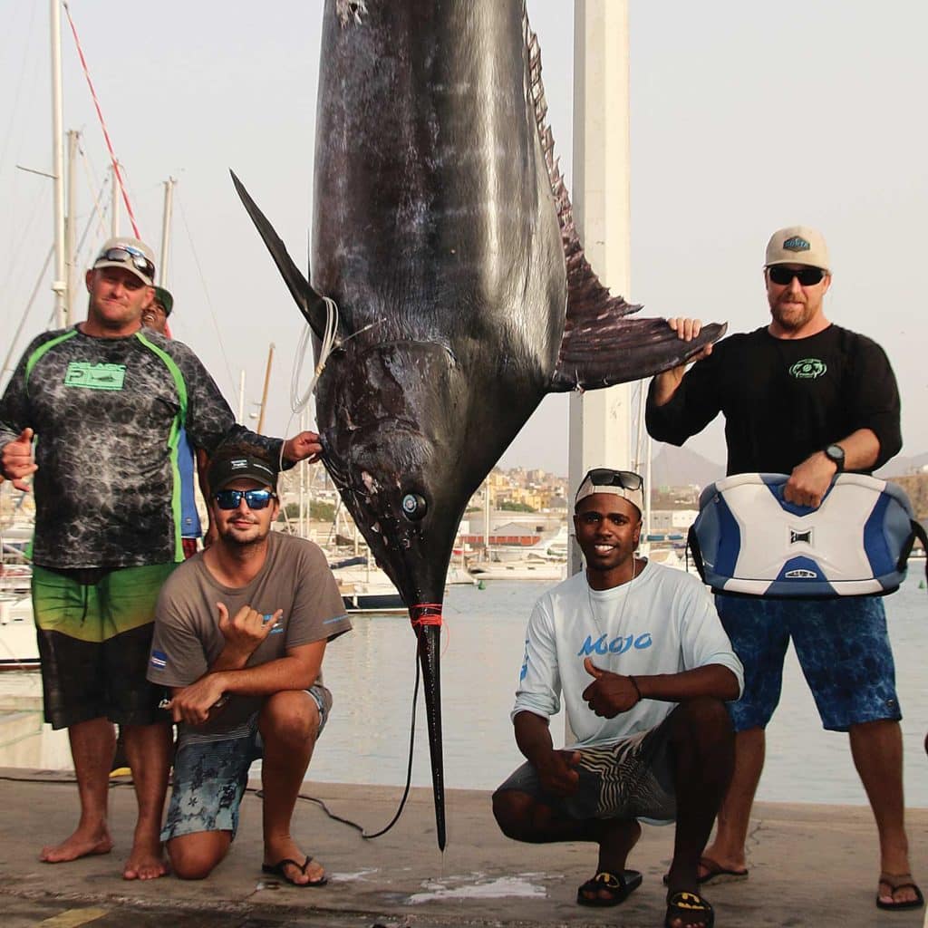 A team of four sport-fishers stand next to a large blue marlin.