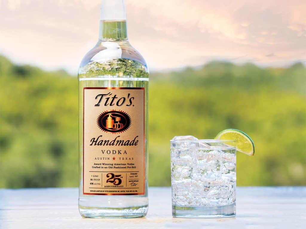 A bottle of Tito's Handmade Vodka next to a cocktail glass.