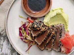 Slices of sesame-encrusted sliced tuna on a plate garnished with slaw and edamame hummus.