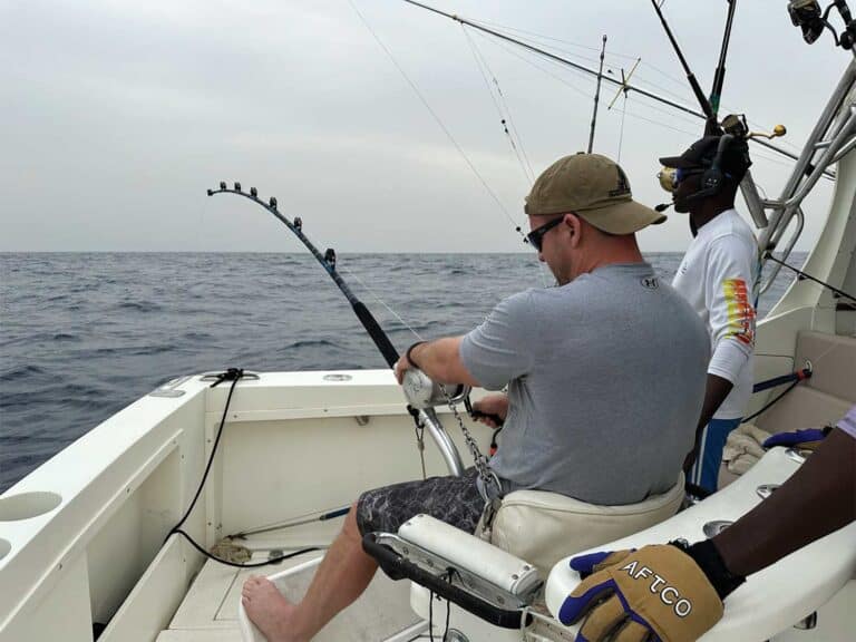 An angler seated in the fighting chair of a sport-fishing boat, fighting a fish on the leader.