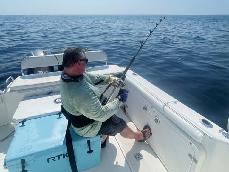 A single angler sits in the fighting chair of a sport-fishing boat cockpit.