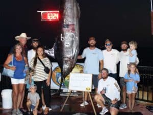 A sport-fishing team stands next to a large 632 pound marlin caught at PIBT. An American flag waves in the wind.