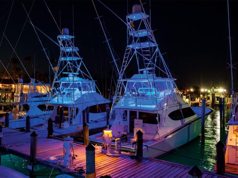Two sport-fishing boats docked at night, lit up by a variety of exterior lights.