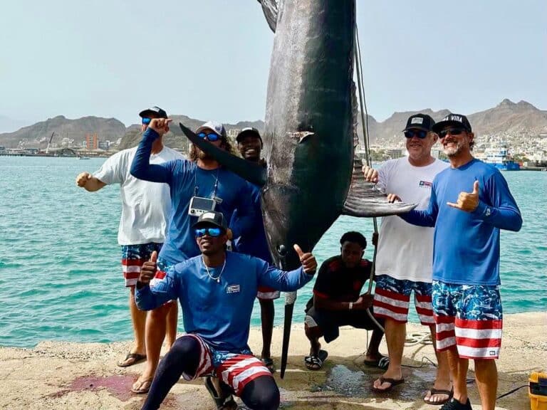 The Dogs Bollocks team standing on a dock weigh-in station, standing around a marlin strung up.