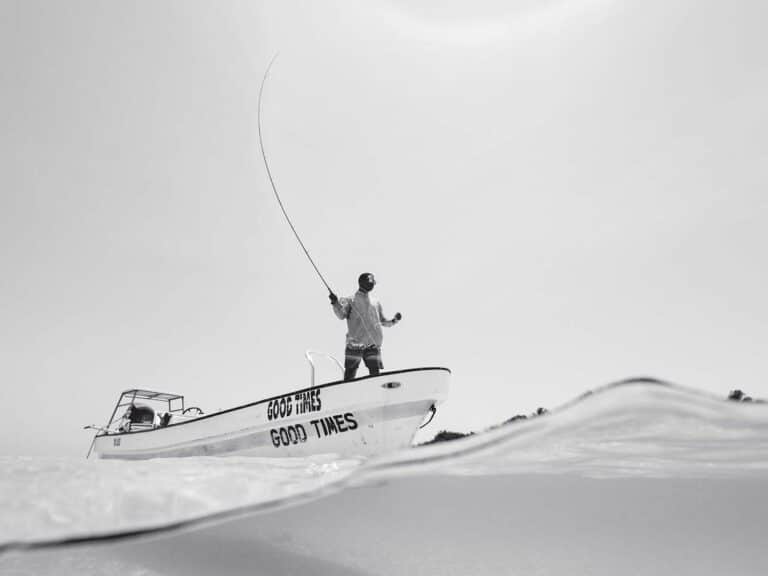 A black and white image of an angler flyfishing from a small boat.