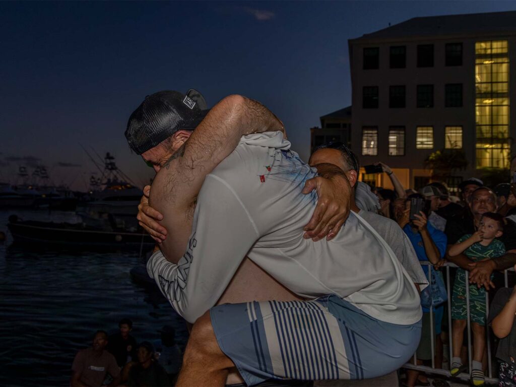 Two anglers hug in celebration on the docks of a marina at night.