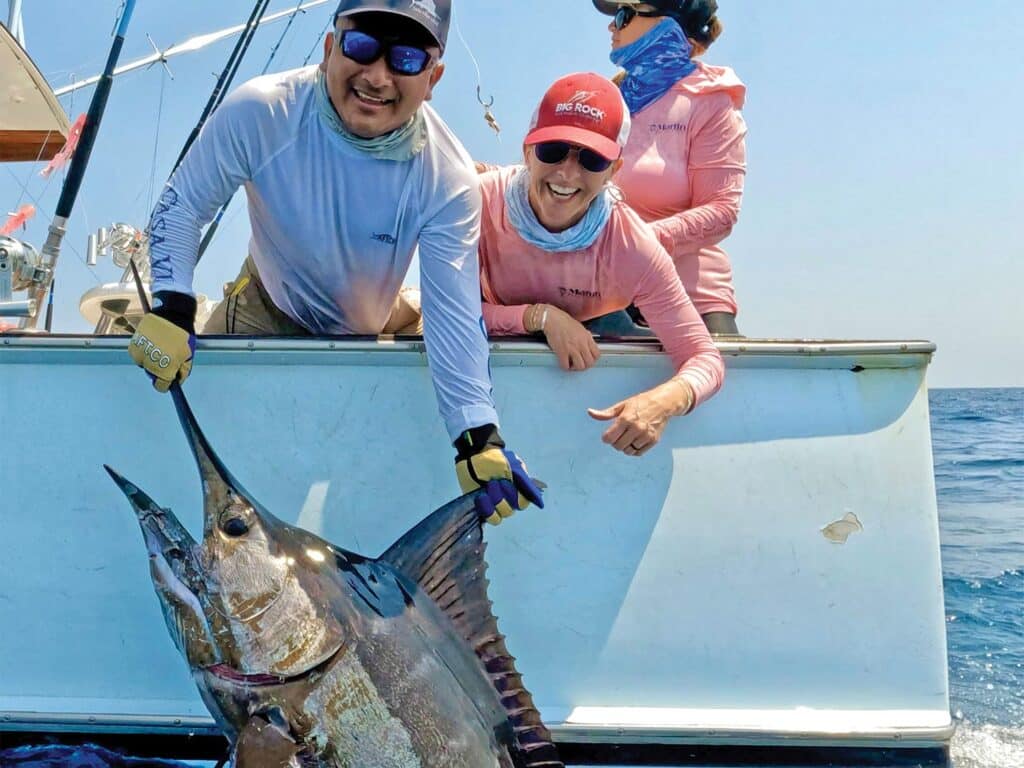 Un miembro de la tripulación ayuda a un pescador a capturar un marlin grande para posar para una fotografía antes de liberarlo.