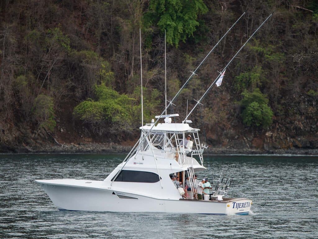 A sport-fishing boat cruises across the water. Lush islands can be seen on the shoreline.