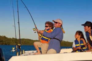 A father and son reel a fish in together while a mom and daughter look at them.