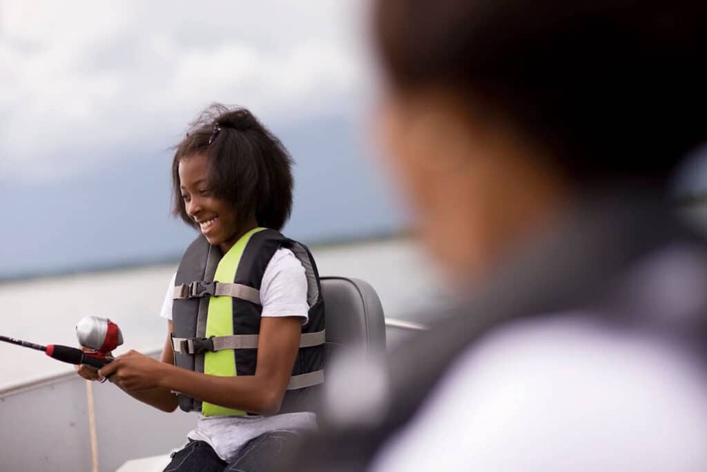 A young girl wearing a life jacket fishing from a boat.