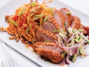 A plate of crispy skin duck breast on a plate next to a side of salad.