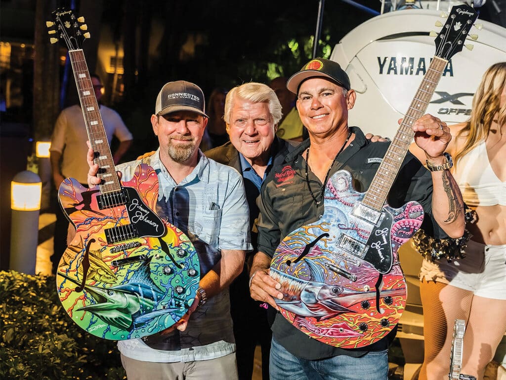 Three men stand for the camera and pose by holding up two custom-painted guitars.