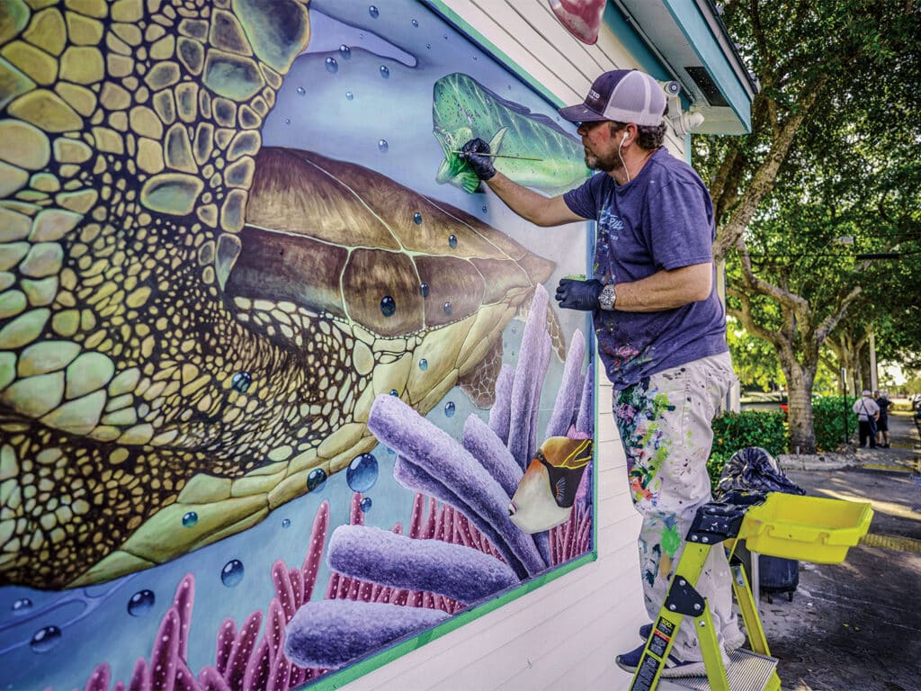 Dennis Friel painting a mural of a sea turtle on an outdoor wall.