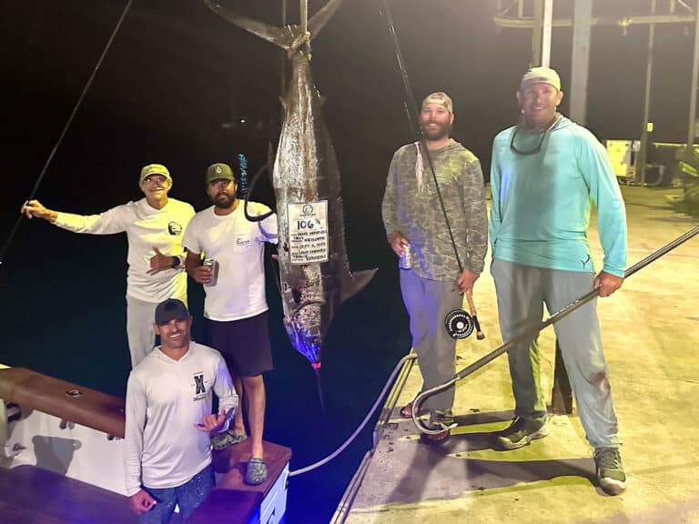 Sport-fishing anglers, captain, and crew stand next to a weighed blue- marlin.