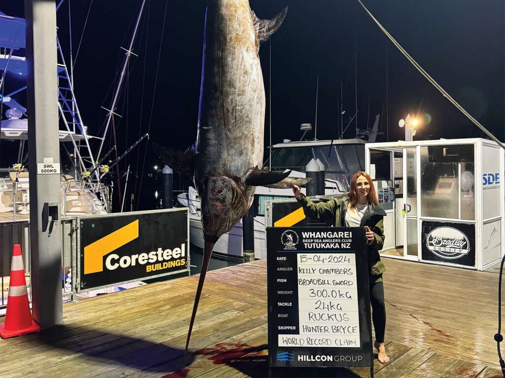 Author Kelly Chambers standing next to a swordfish being weighed in at a dockside station.