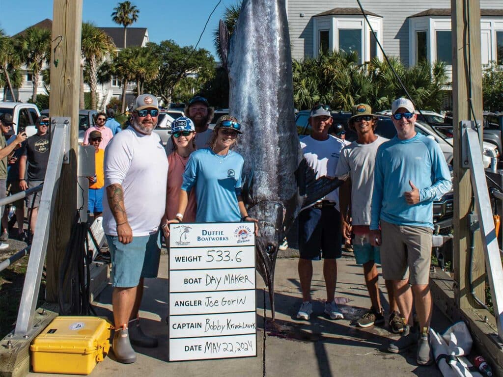 A sport-fishing team next to a large marlin being weighed