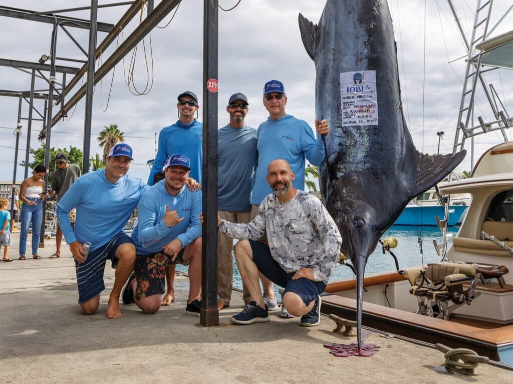 A team of sport-fishing anglers pose next to a large marlin being weighed dockside. A sign on the marlin reads "1081 1/2 punds"