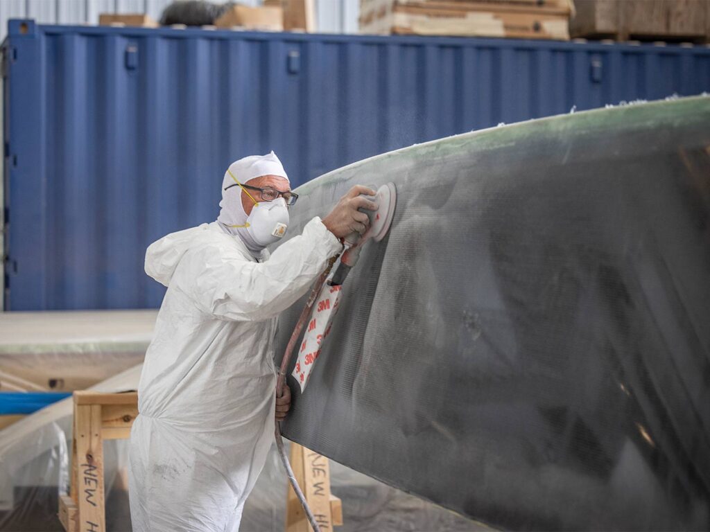 A boat builder sanding a sport-fishing boat hull.