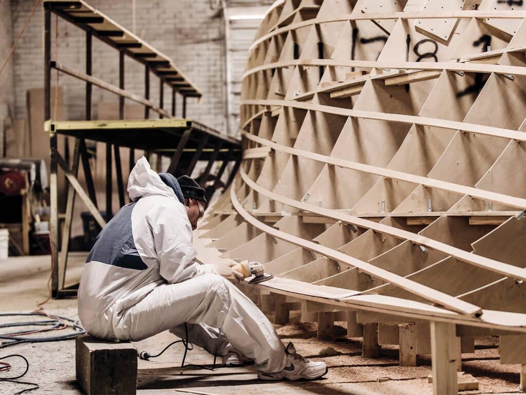 A boat builder puts sanding touches on a boat hull build.