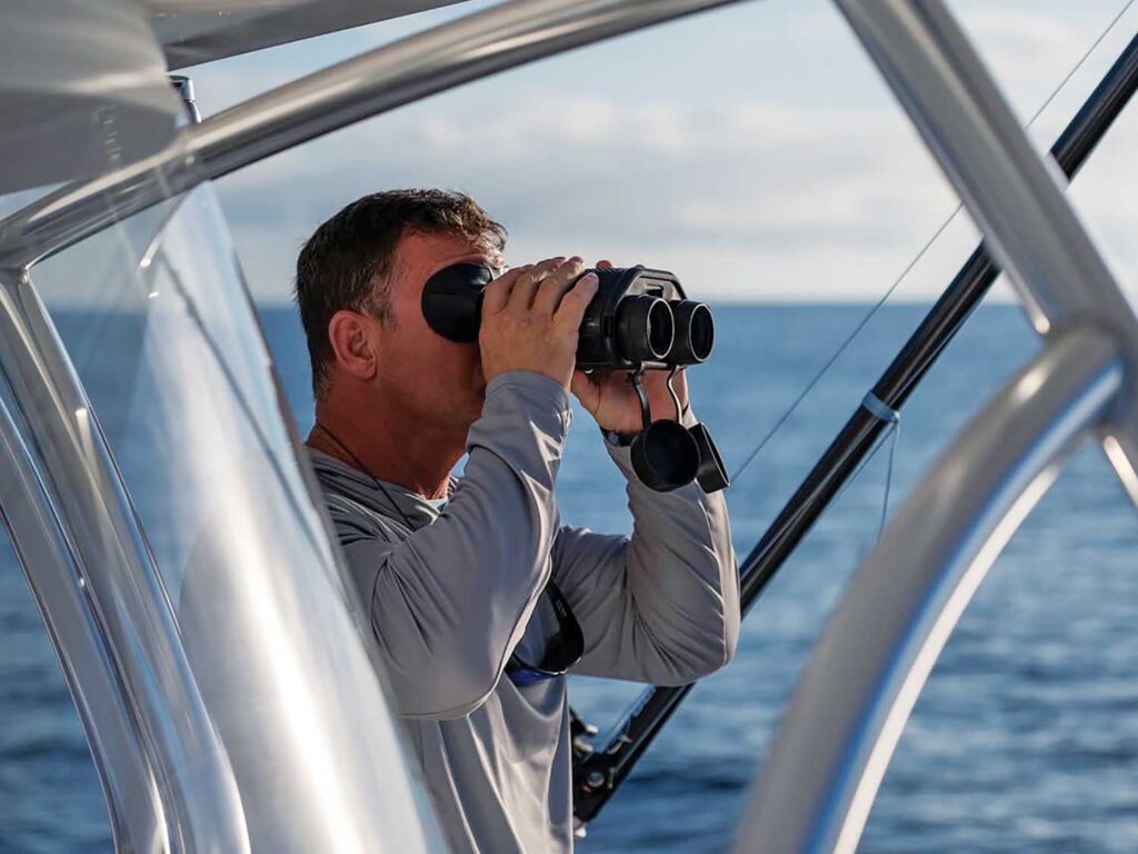 A crewmate uses binoculars to scan the horizon.