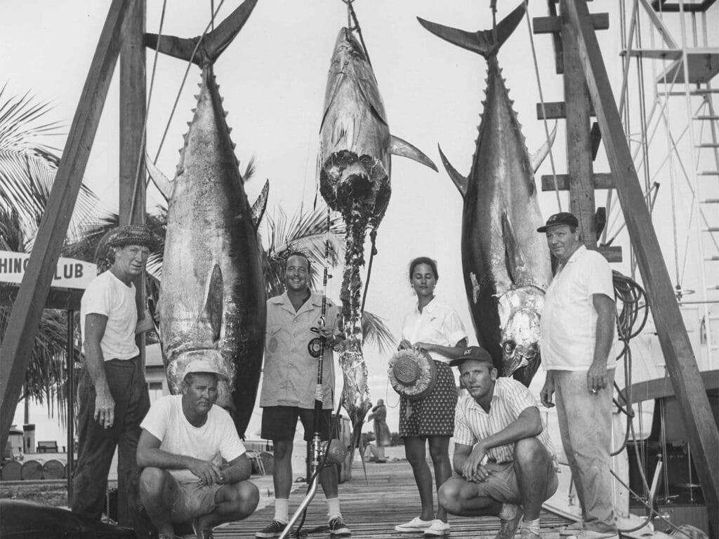 A black and white image of anglers standing beside weighed tuna.