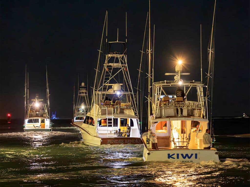 A fleet of sport-fishing boats cruising on the ocean at night.