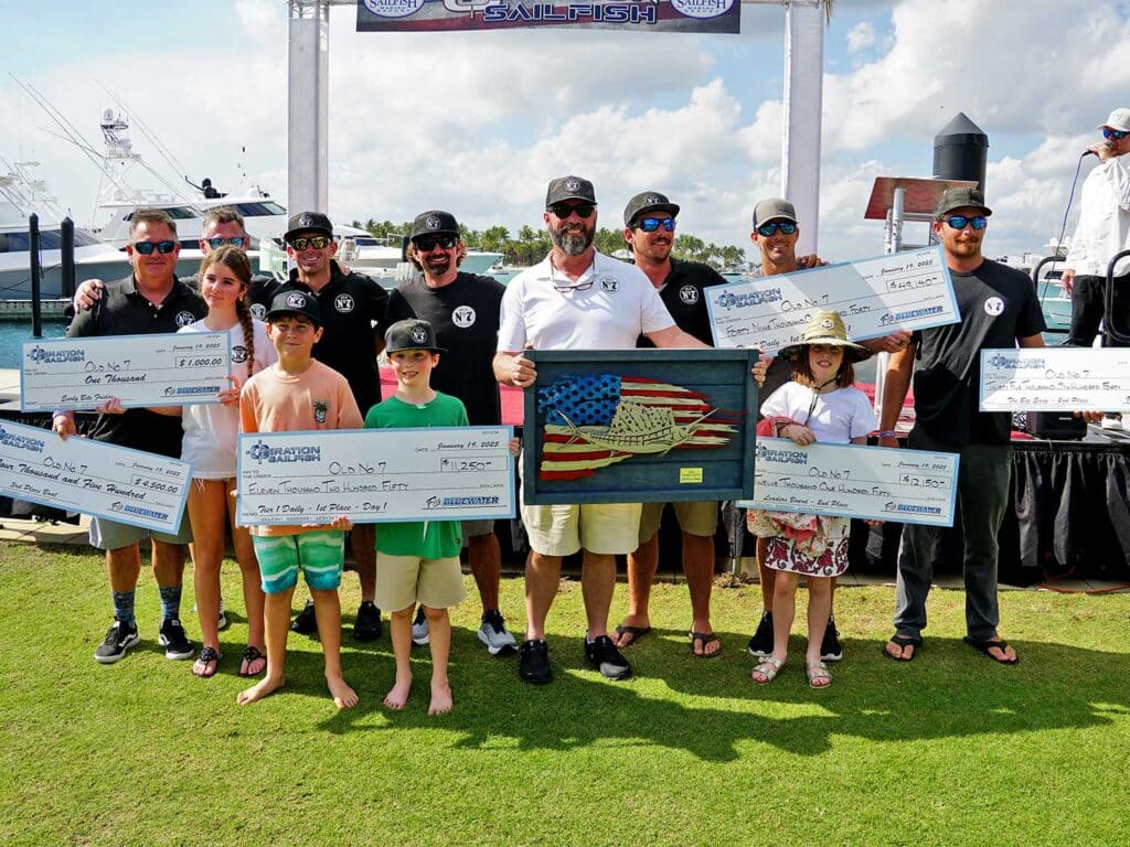 Team Old No. 7 stand at the awards ceremony holding oversized checks.