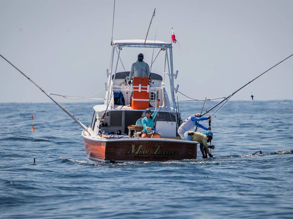 An angler sits in the fighting chair and holds up her hand in celebration.