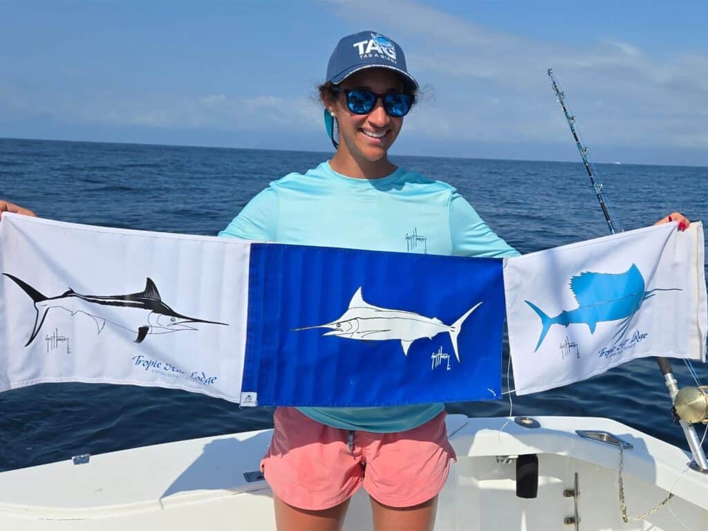 An angler smiles as she holds up three release flags. One for black marlin, one for white marlin, and one for sailfish.